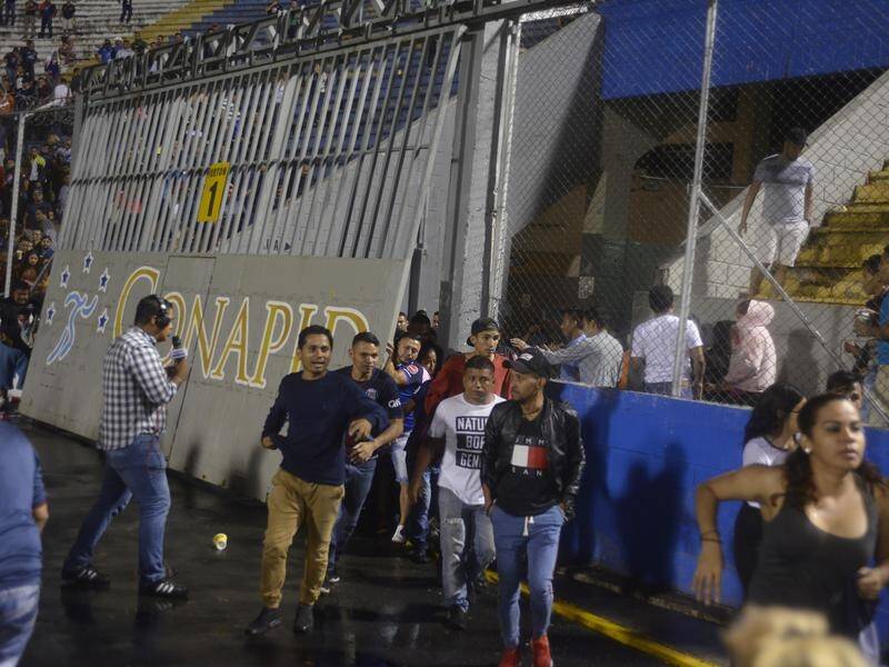 Soccer fans run from tear gas fired by police to break up deadly riots at a Honduran soccer match. .